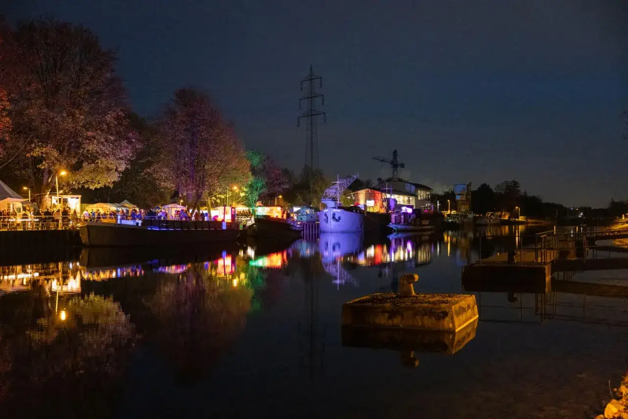 Buntes Lichtermeer am weihnachtsmarkt schiffshebewerk henrichenburg. Boote und Bäume spiegeln sich im Wasser.