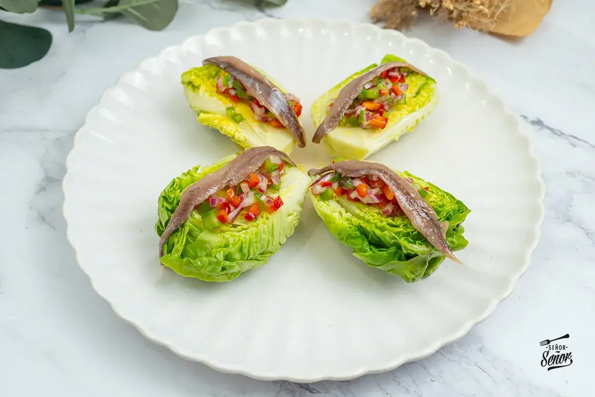 Cuatro cogollos de lechuga rellenos de pimientos y cebolla picados, coronados con anchoas. Un bocado fresco y sabroso.