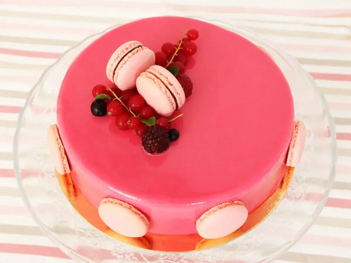 G&acirc;teau rose vif avec une d&eacute;coration entremet fruit rouge : groseilles, m&ucirc;res, framboises et macarons roses.