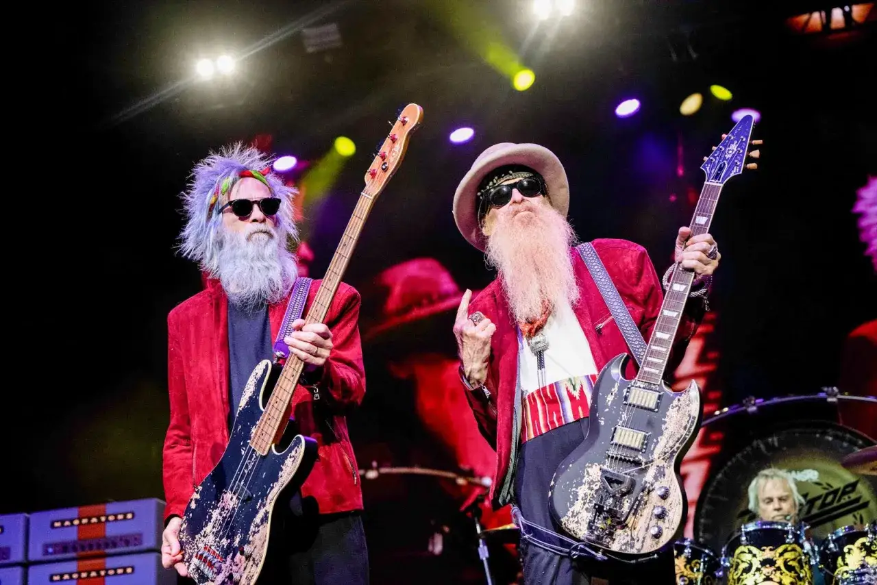 ZZ Top członkowie na scenie: Billy Gibbons z gitarą i Dusty Hill z basem, obaj w czerwonych marynarkach i z charakterystycznymi brodami.