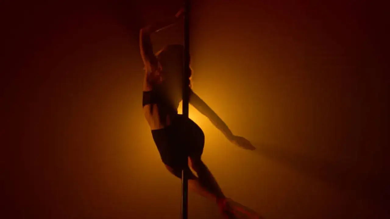 Kobieta w czarnym stroju wykonuje taniec na rurze, tworząc zmysłową choreografię. To może być inspiracja, jak zrobic striptiz.