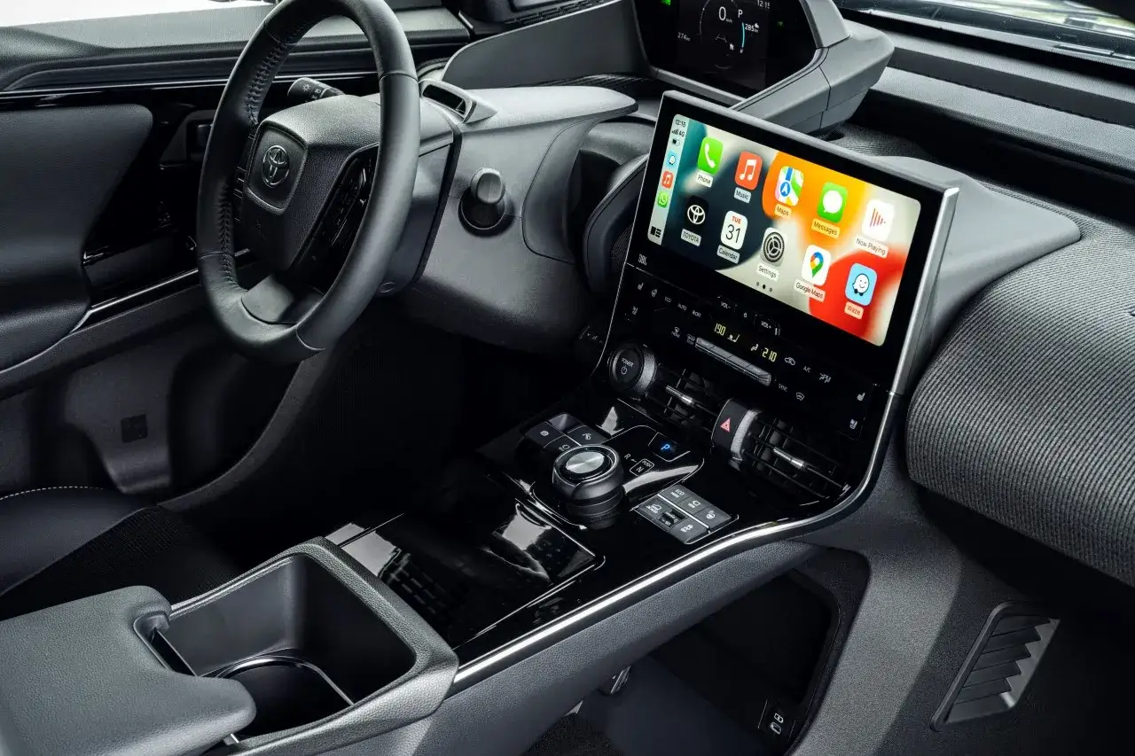 Wnętrze Toyoty bz4x z ekranem multimedialnym Apple CarPlay. Kierownica, konsola środkowa i siedzenie.
