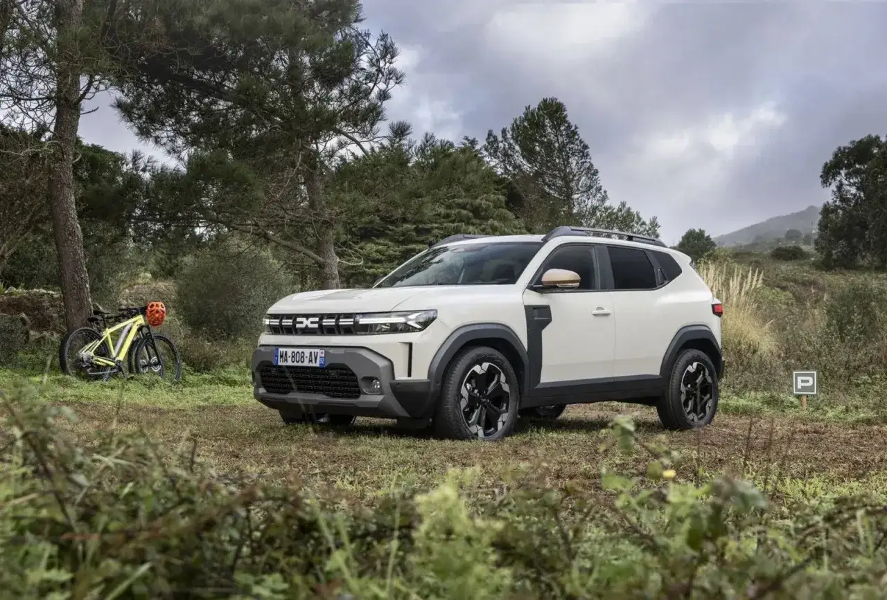 Biały Dacia Duster 1.6 benzyna zaparkowany na leśnej polanie obok żółtego roweru górskiego.