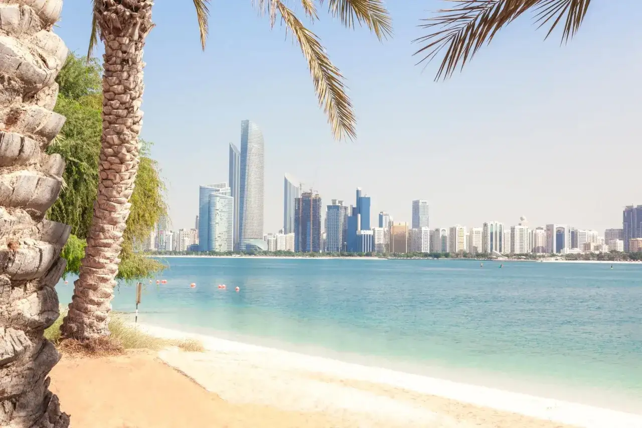Palmy nad turkusową wodą, z widokiem na nowoczesną panoramę miasta Abu Zabi. Idealne miejsce na relaks na corniche Abu Dhabi.