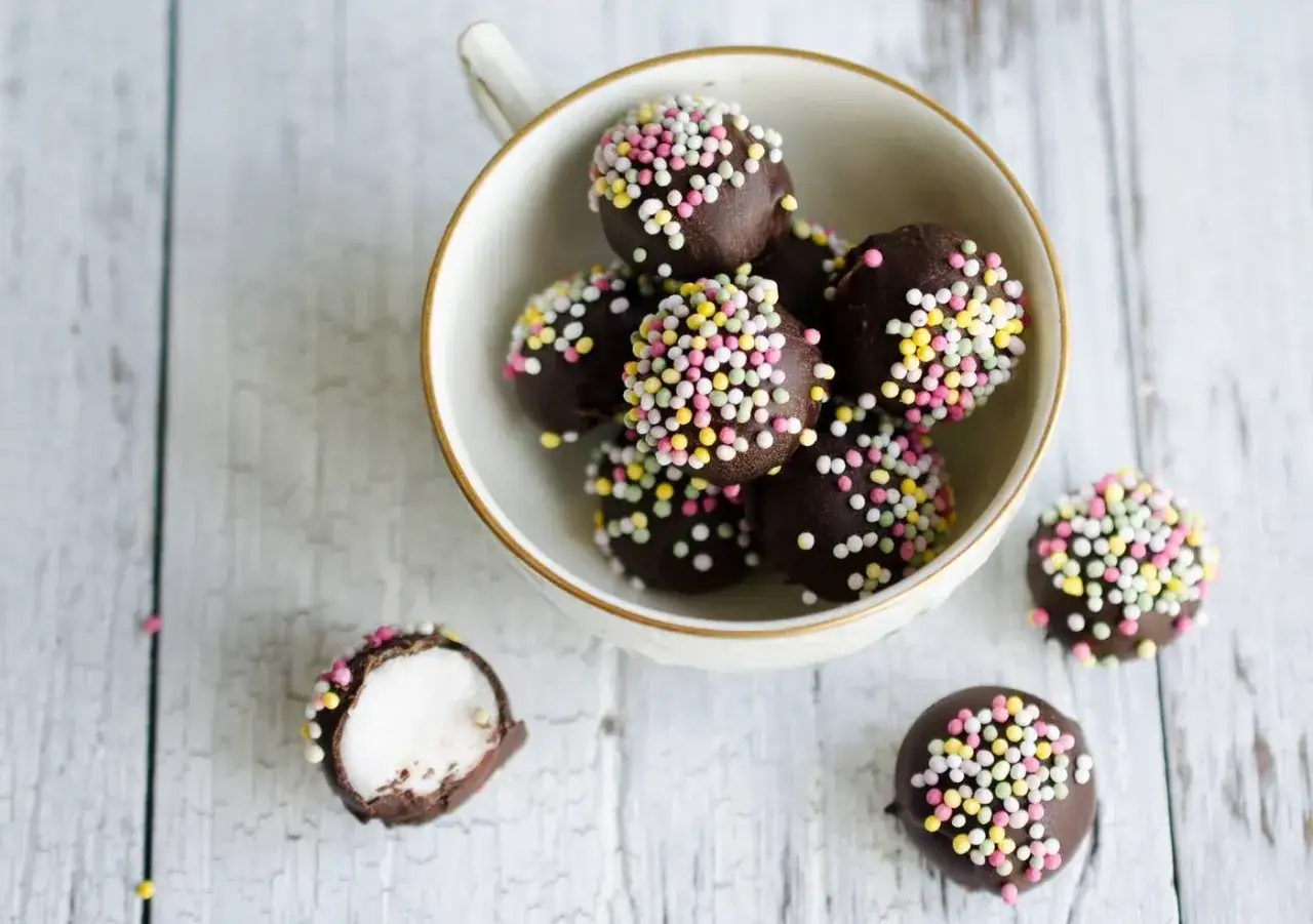 Chokladbollar med färgglatt strössel, perfekta för ett enkelt punschpraliner recept. En är uppskuren och visar ett vitt inre.