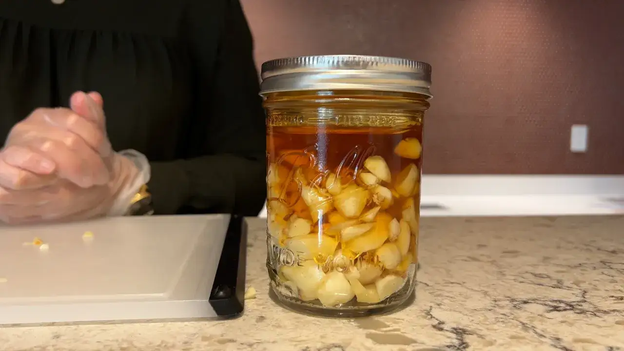 Ein Glas mit Zwiebeln, Honig und Saft. Die Zwiebeln sind in einer goldenen Flüssigkeit eingelegt, die wie Honig aussieht.