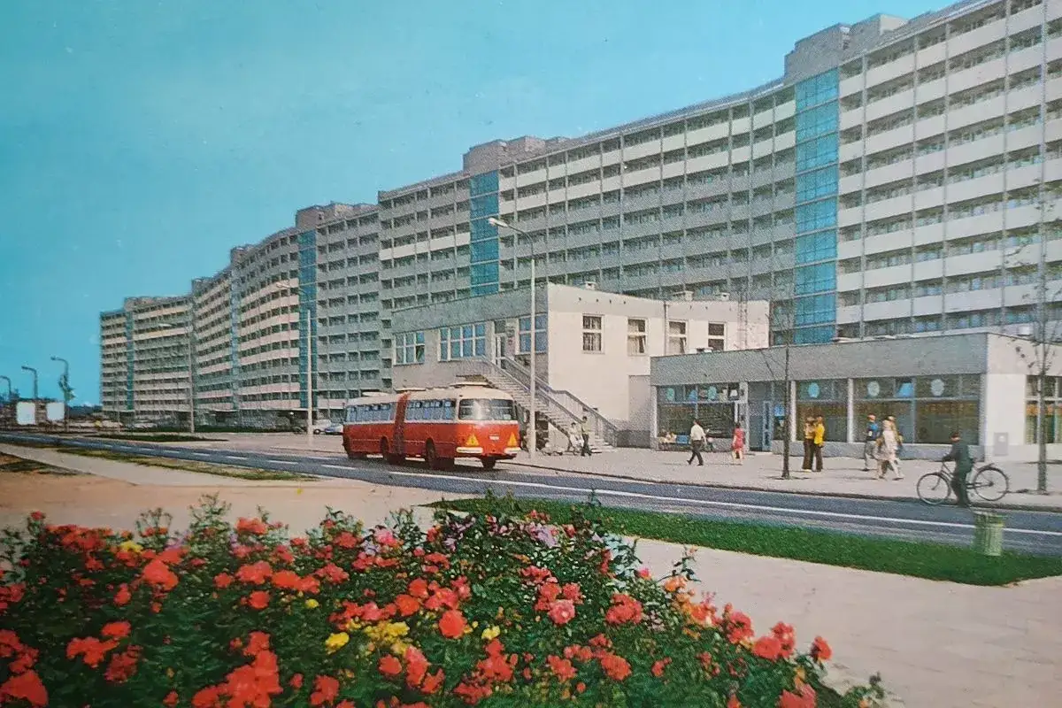 Falowiec w Gdańsku, długa, falująca bryła architektoniczna, z czerwonym autobusem i kwitnącymi krzewami róż.