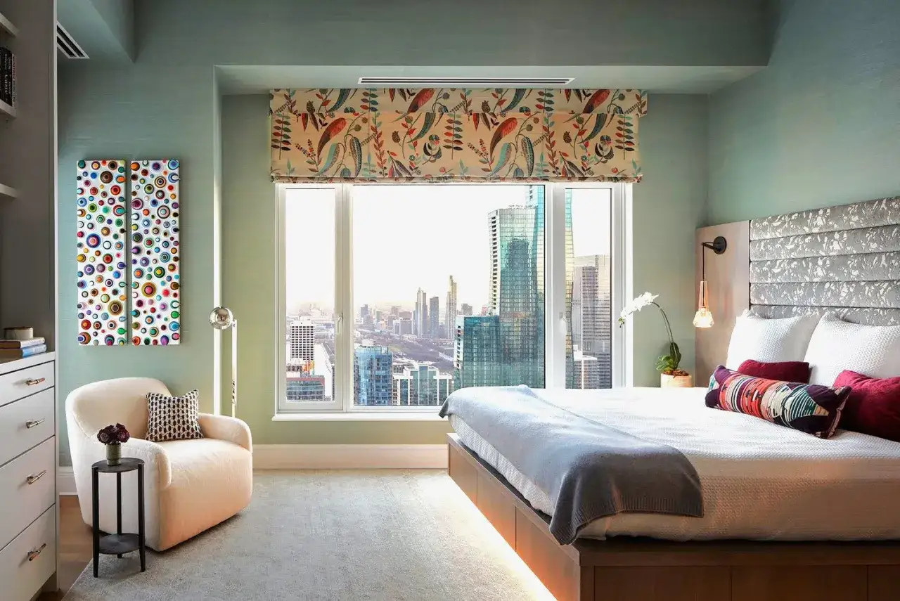 Een modern **bed voor raam** met uitzicht op de skyline. Een comfortabele fauteuil en kleurrijke kunst aan de muur maken de kamer compleet.