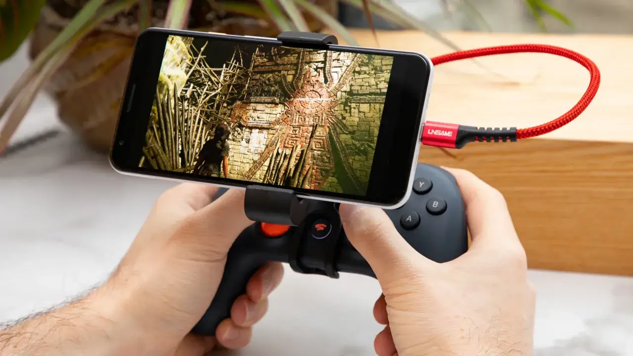 Ręce trzymają smartfon z grą przygodową, podłączony kablem do kontrolera. To idealne rozwiązanie do grania w gry na **stadia**.