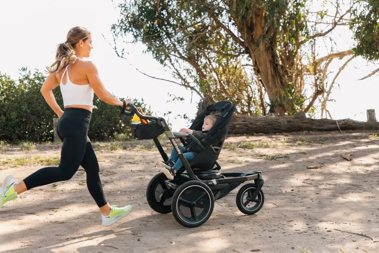 Eine sportliche Frau joggt mit ihrem Baby im Kinderwagen. Sie genießt das Joggen nach der Geburt in der Natur.