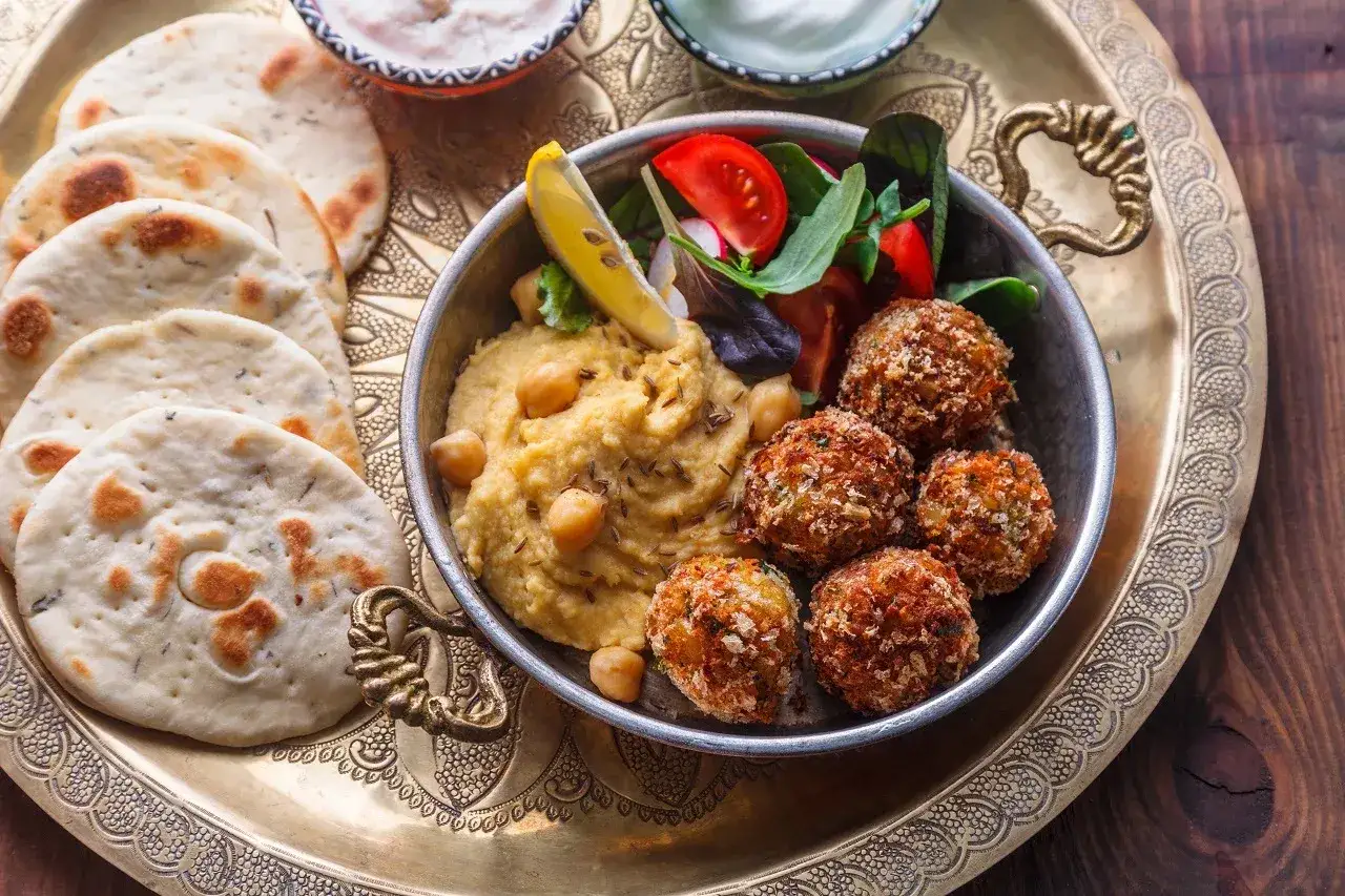 Pyszne jedzenie koszerne: hummus, falafel, świeże pieczywo i sałatka na ozdobnej tacy.