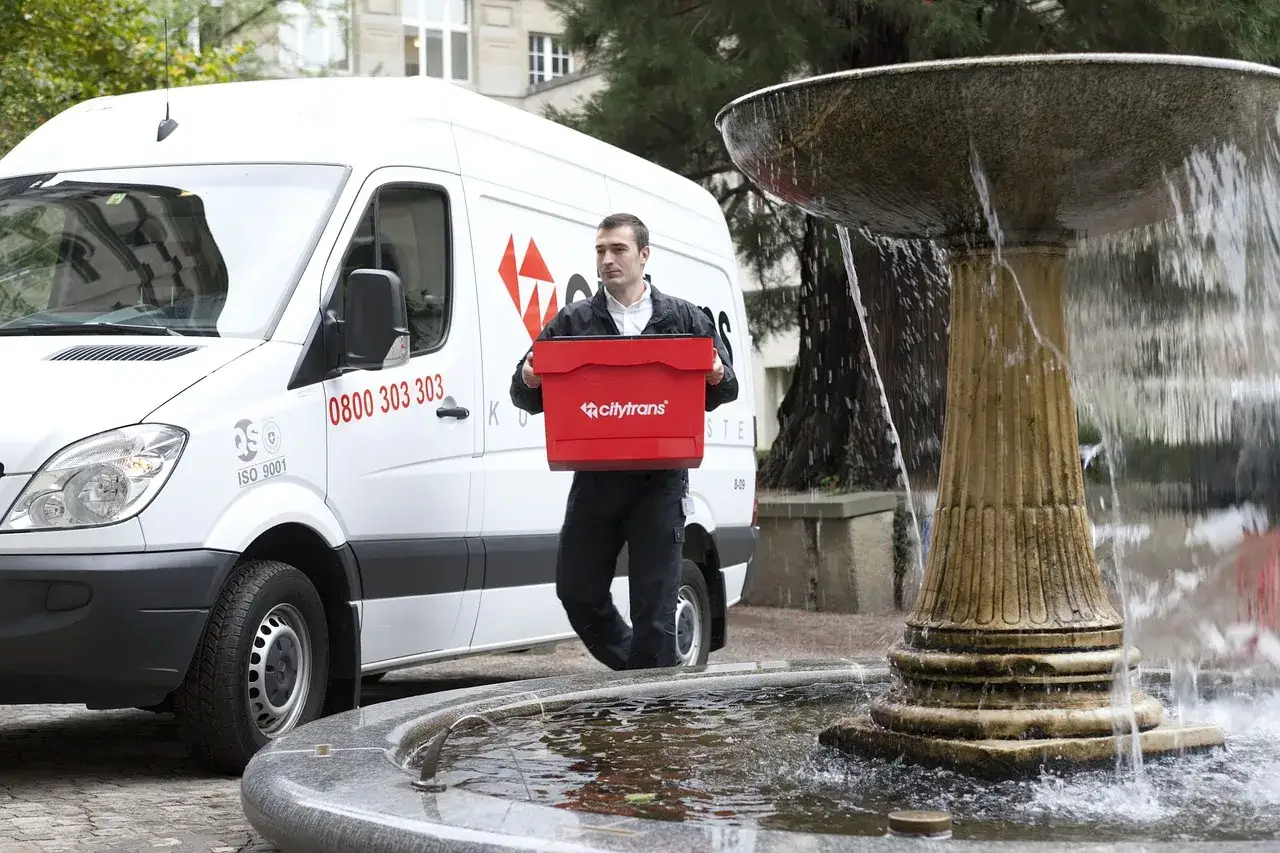 Kurier Citytrans z czerwonym pojemnikiem obok fontanny. Zastanawiasz się, ile zarabia kurier?