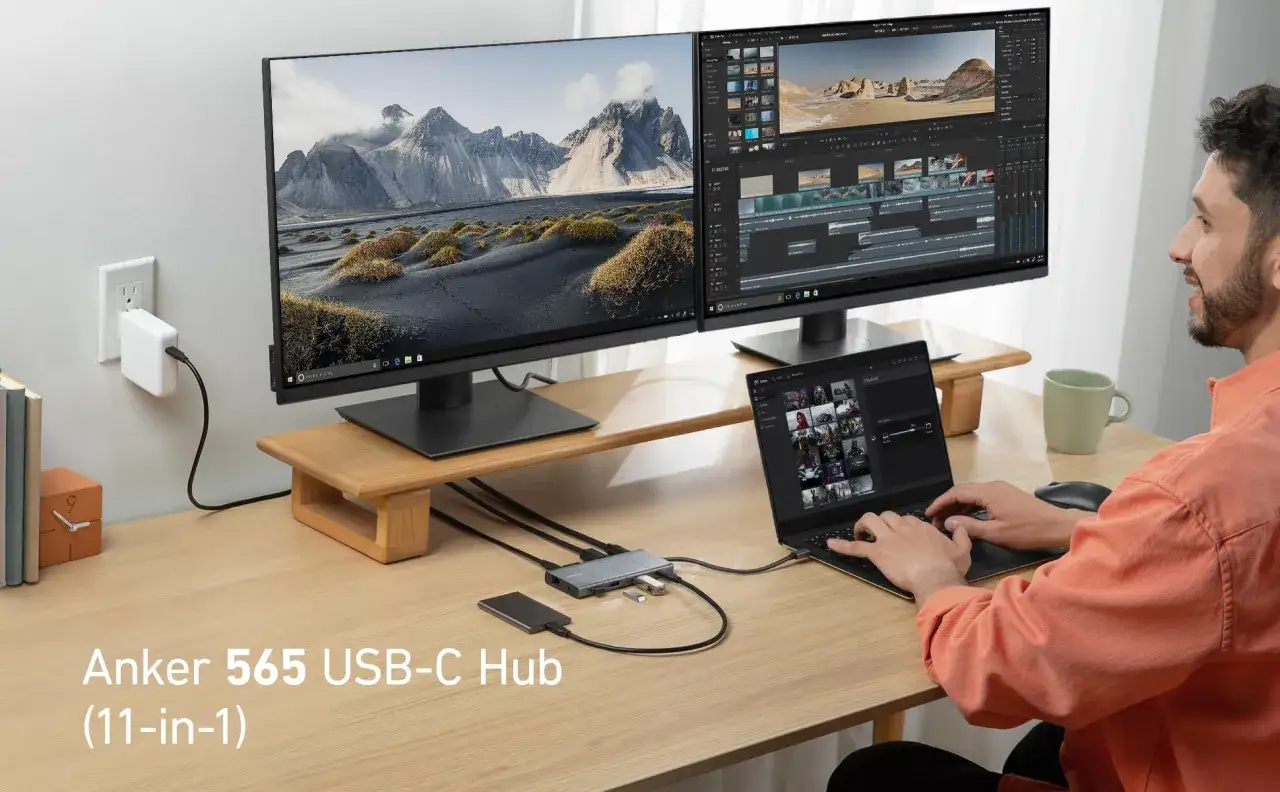 Mężczyzna pracuje przy biurku, korzystając z laptopa i dwóch monitorów. Używa hubu USB-C do udostępniania ekranu i rozszerzania możliwości swojego stanowiska pracy.