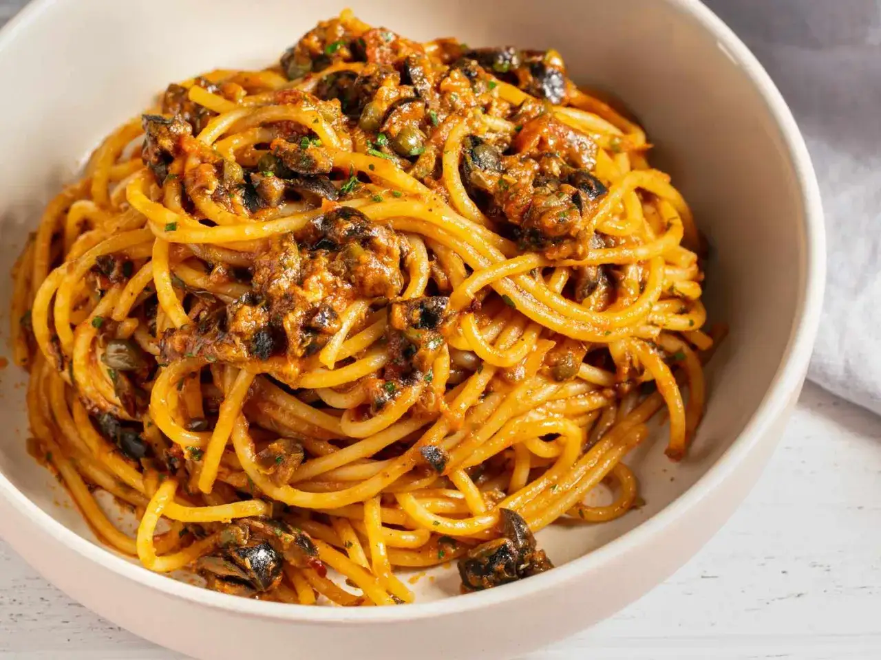 Eine Sch&uuml;ssel voller Spaghetti Puttanesca, mit einer w&uuml;rzigen Sauce aus Tomaten, Oliven und Kapern.
