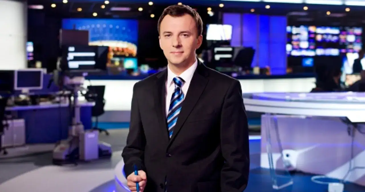 Krzysztof Górlicki w garniturze stoi w studiu telewizyjnym z niebieskimi ekranami w tle.