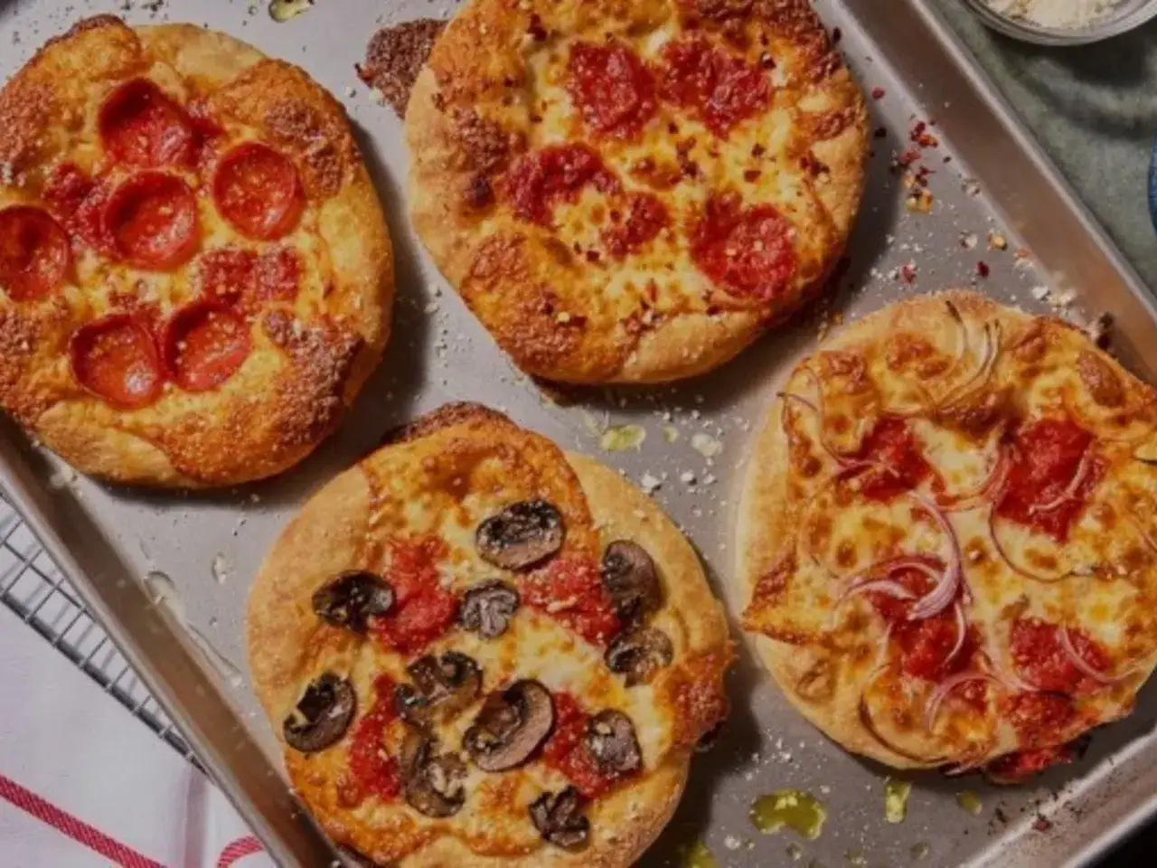 Cuatro mini pizzas recién horneadas en una bandeja: una con pepperoni, otra con champiñones y dos con pepperoni y cebolla. ¡Perfectas para compartir!