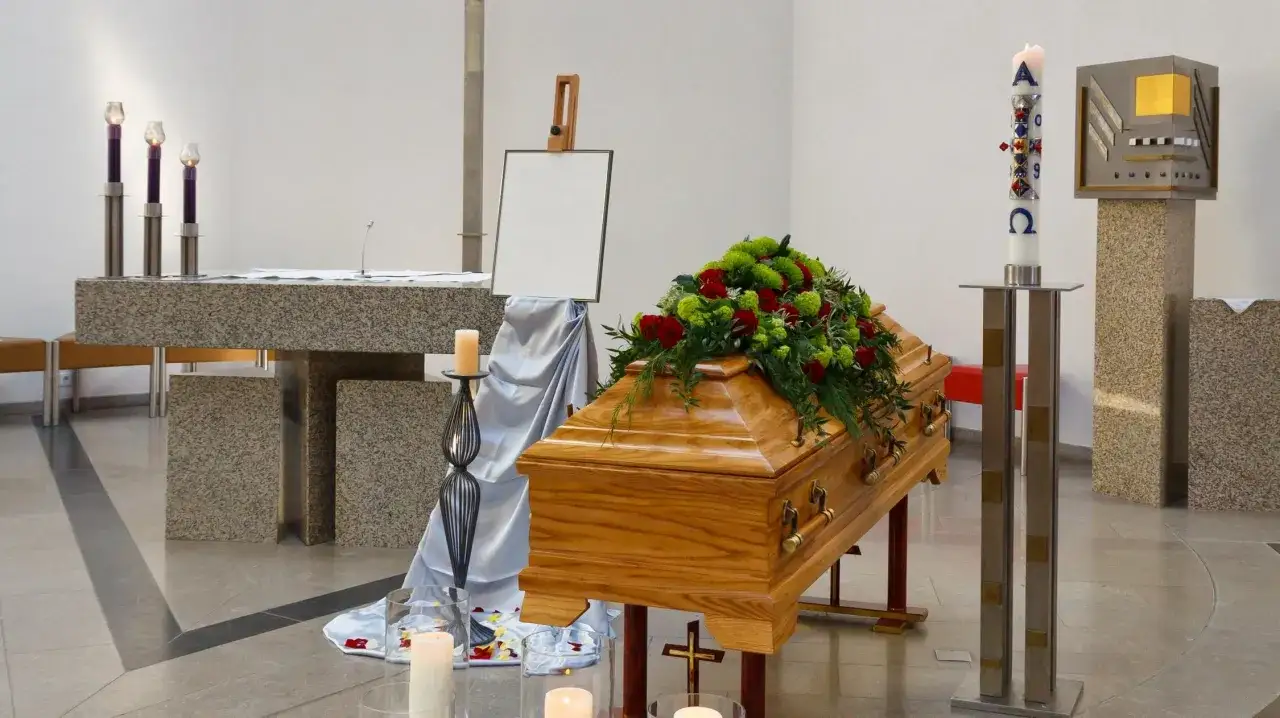 Drewniana trumna z kwiatami, świece i krzyż. Zastanawiasz się, ile się zarabia w zakładzie pogrzebowym?