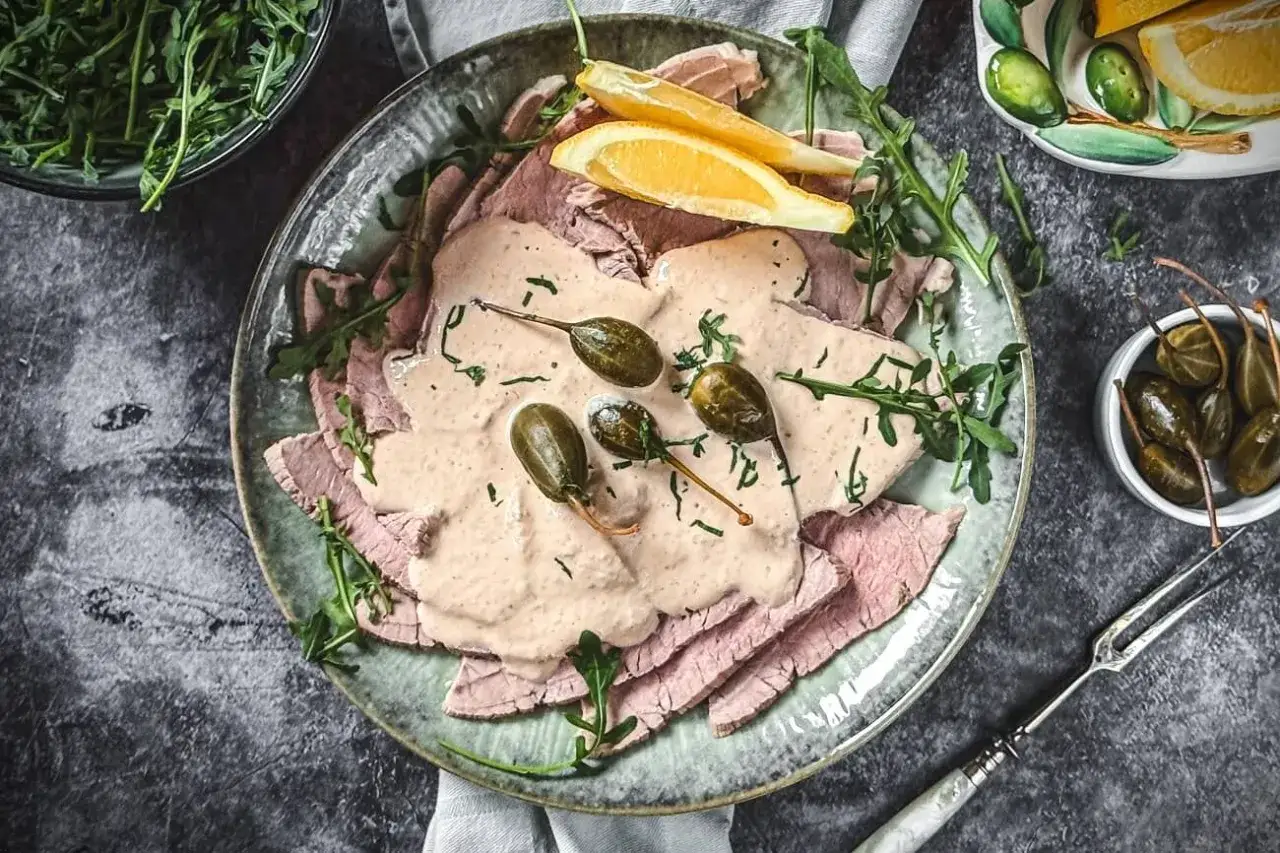 Vitello Tonnato Rezept: D&uuml;nne Kalbfleischscheiben mit cremiger Thunfischsauce, Kapern und Zitronenspalten auf einem Teller.