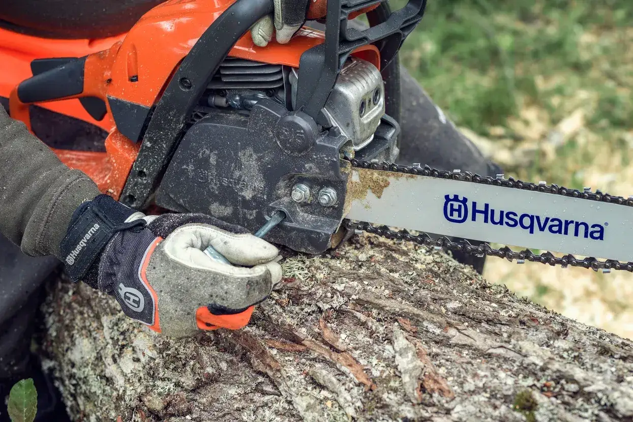 Dłoń w rękawicy reguluje piłę łańcuchową Husqvarna 135. Dane techniczne tej maszyny są kluczowe dla jej efektywnego użytkowania.