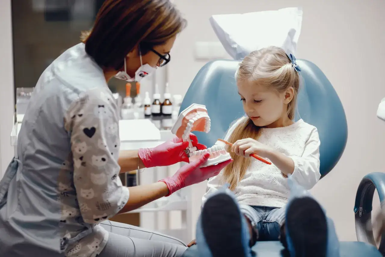 Dentystka pokazuje dziecku, jak zamaskować brak zęba domowe sposoby, używając modelu szczęki i szczoteczki.