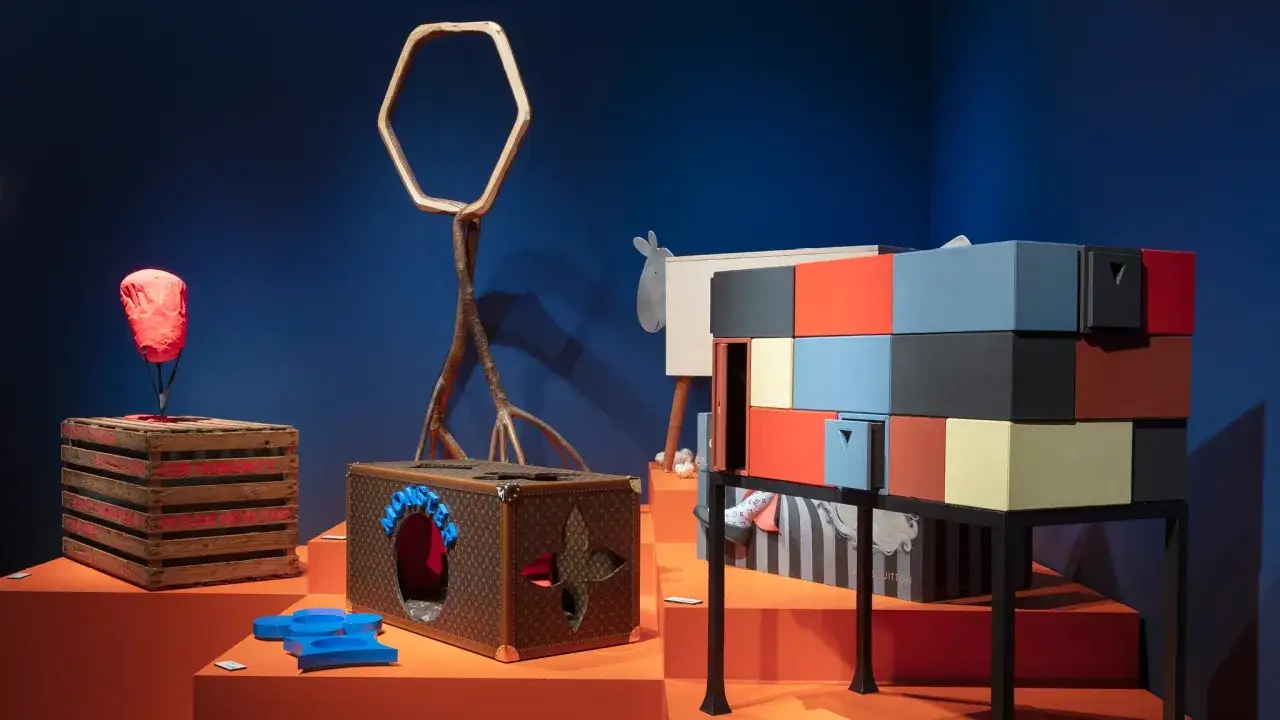 Esposizione di oggetti d'arte, tra cui una cuccia per cani in tela monogram Louis Vuitton, che evoca le origini del brand.