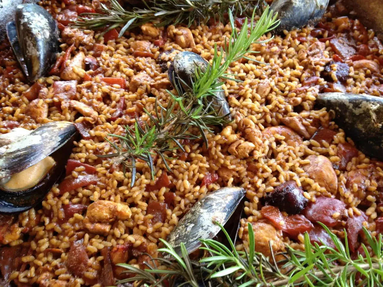 Paella mixta reci&eacute;n hecha, con arroz dorado, trozos de pollo, mejillones y pimientos rojos, decorada con ramitas de romero fresco.