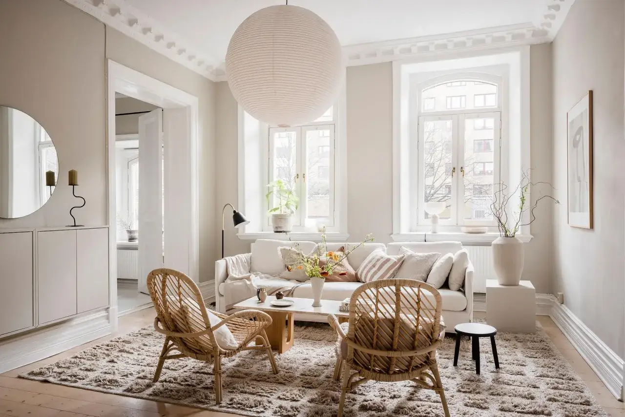 Ein gemütliches wohnzimmer beige grau weiss mit Rattanstühlen, einem Sofa und einem großen Teppich.