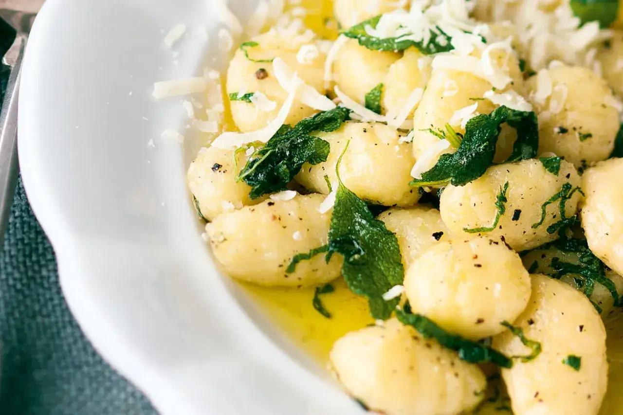 Gnocchi Nudeln in Butter mit Salbeiblättern und geriebenem Parmesan, serviert in einer weißen Schüssel.