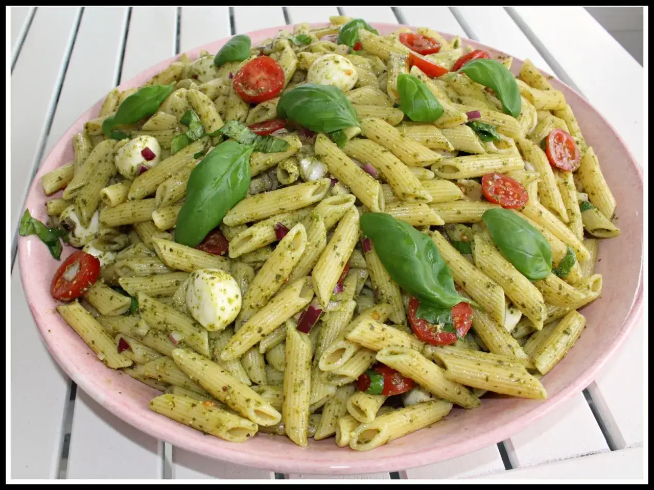 En stor skål med pastasallad med penne, pesto, körsbärstomater, mozzarella och basilika. En perfekt pastasallad pesto för sommaren.