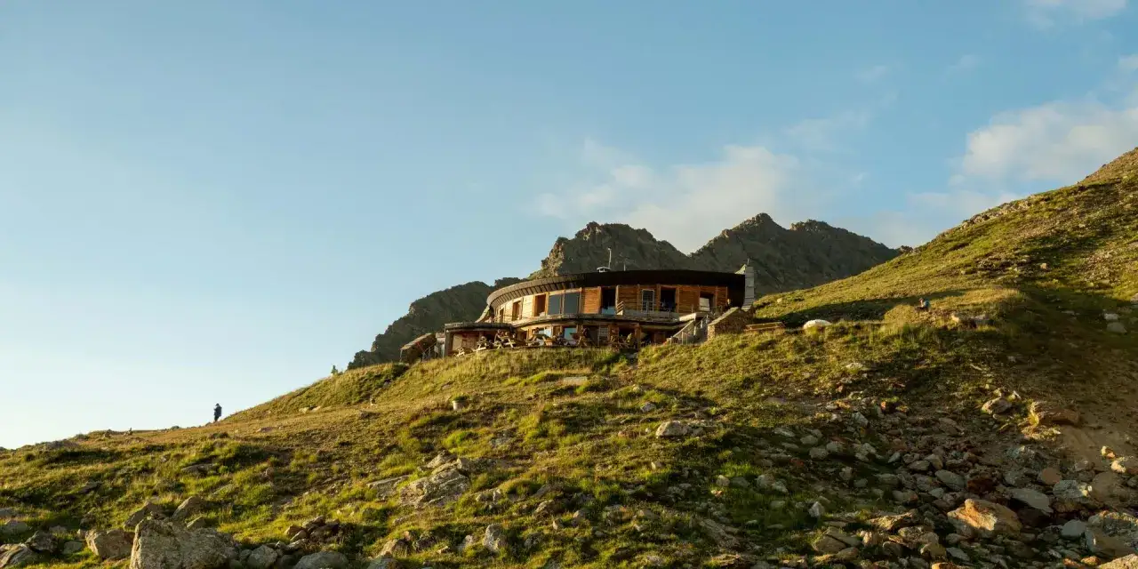 Un refuge moderne sur une cr&ecirc;te rocheuse, offrant une vue imprenable. Un randonneur solitaire admire le paysage, pr&ecirc;t pour le refuge tour du mont blanc.