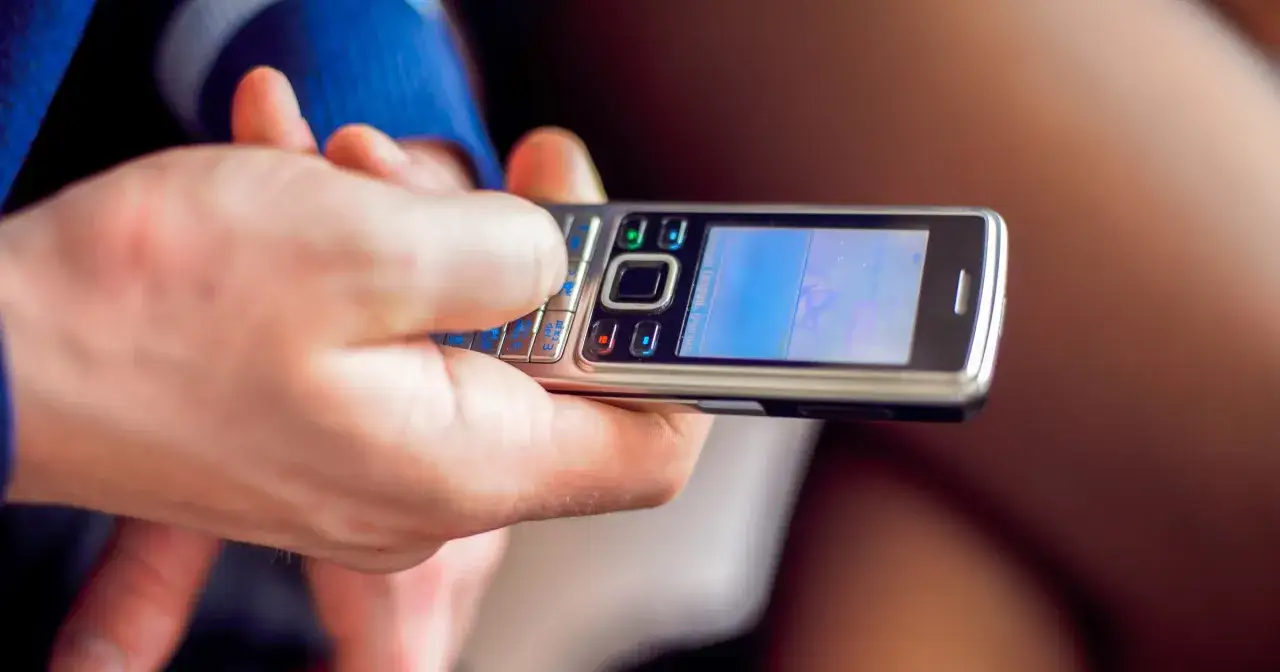 Dłoń pisze SMS-a na starym telefonie z klawiaturą numeryczną, obsługującym sieć 3g.
