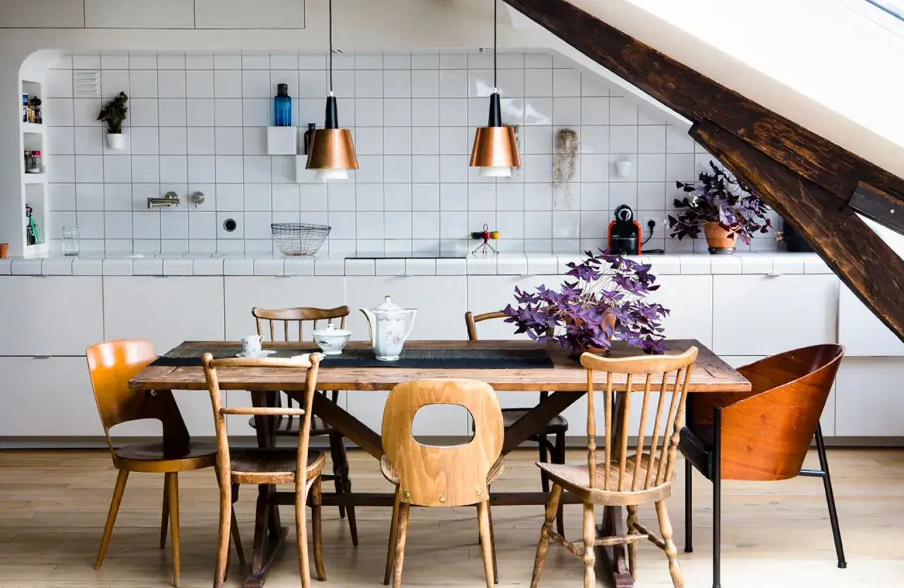 Une cuisine salle à manger en longueur sous un toit mansardé, avec un îlot central en bois et des chaises dépareillées.