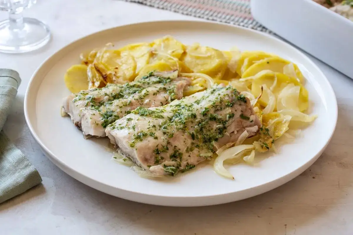 Dos filetes de pescado mero con hierbas y patatas en rodajas.