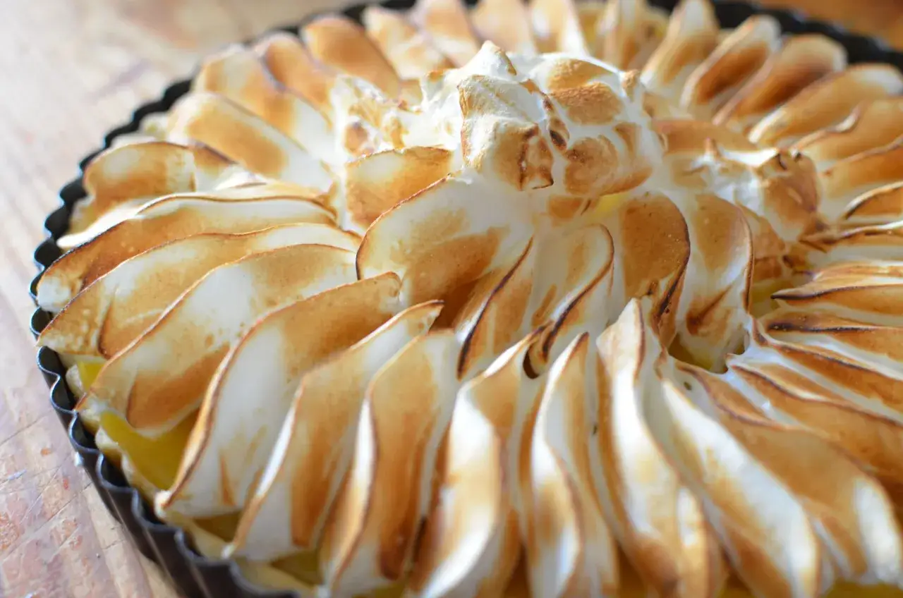 Złocista tarta z lemon curd, ozdobiona puszystą, przypieczoną bezą, wygląda apetycznie.