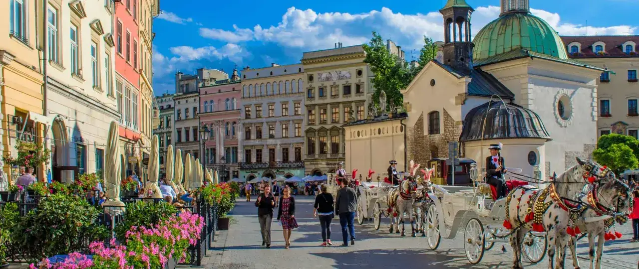 En vacker dag i Krakow, perfekt för en reseguide. Hästdragna vagnar väntar på turister vid färgglada byggnader och blomsterprydda trottoarer.