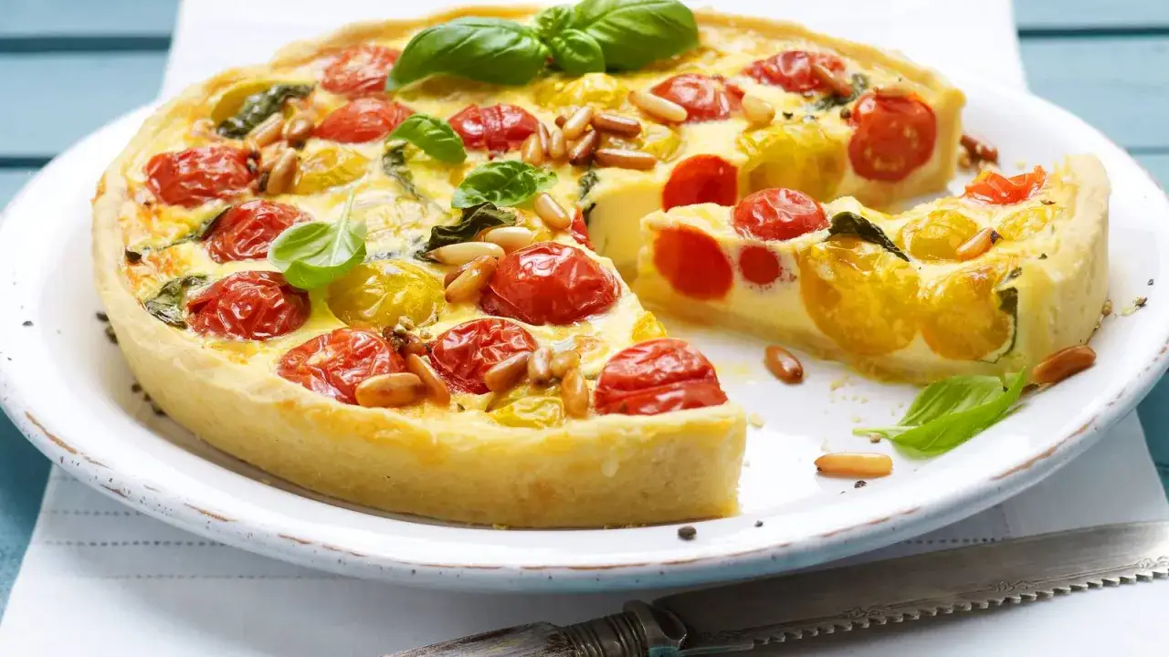 Eine k&ouml;stliche Tomaten-Quiche mit roten und gelben Kirschtomaten, Pinienkernen und Basilikum auf einem Teller.