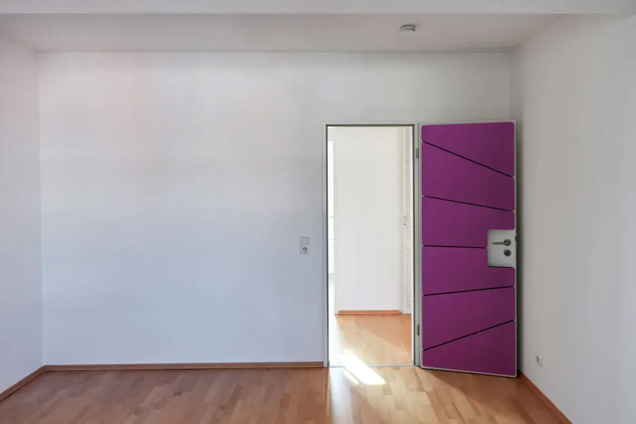 Porte violette ouverte, id&eacute;e pour comment insonoriser une porte. Sol en bois, murs blancs.
