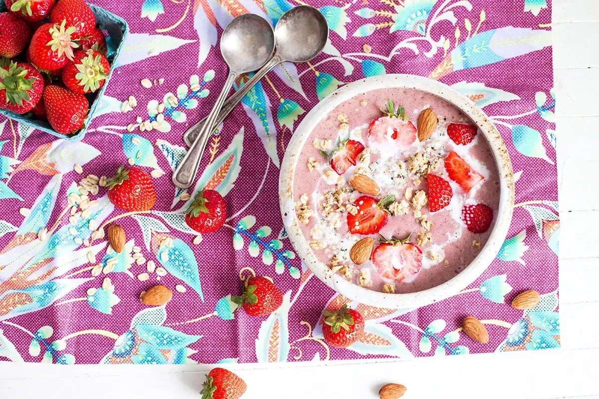 Un délicieux smoothie fraise garni de fruits frais, d'amandes et de granola, prêt à être dégusté.