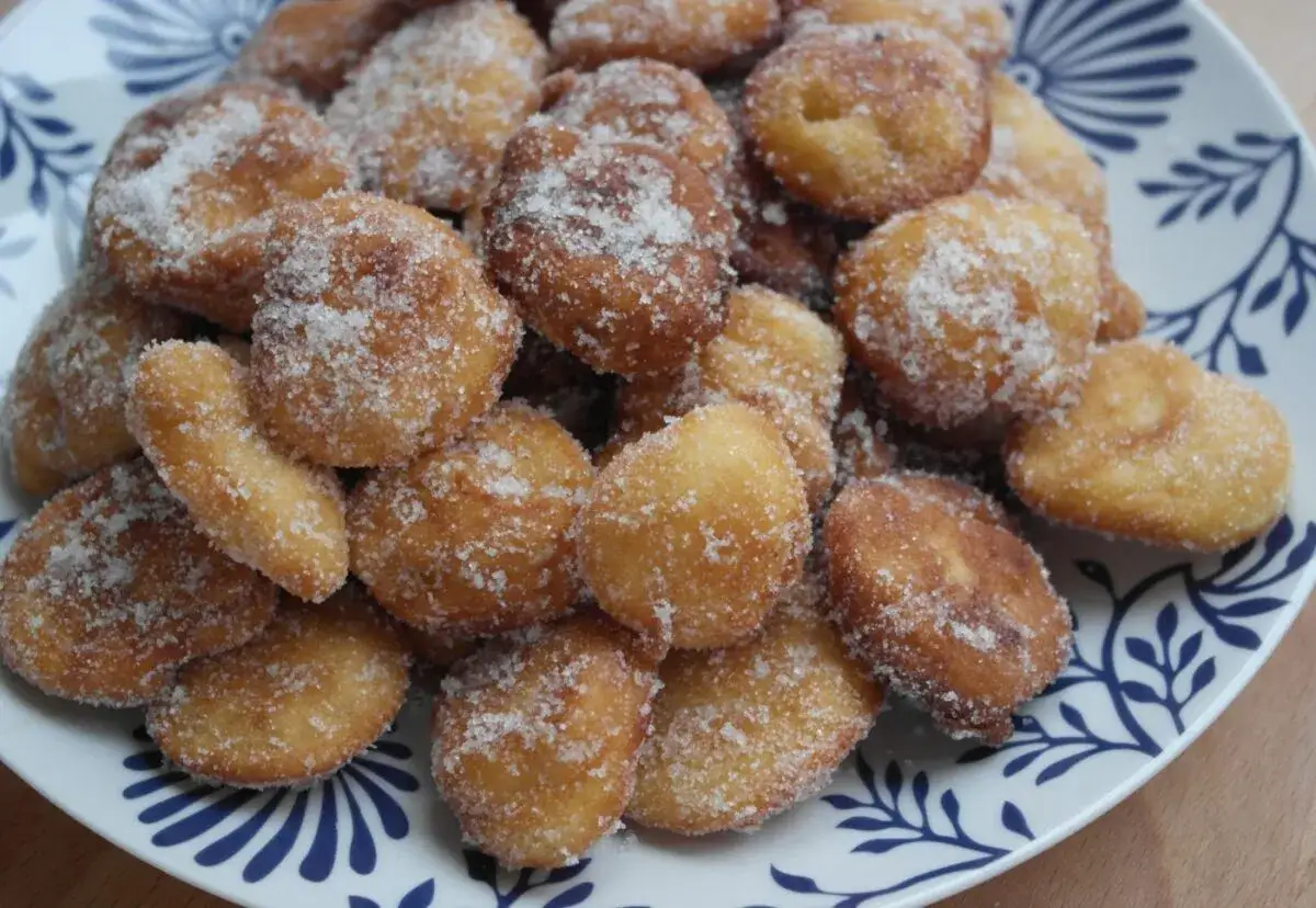 Montón de buñuelos de manzana dorados y espolvoreados con azúcar, servidos en un plato con diseño azul.