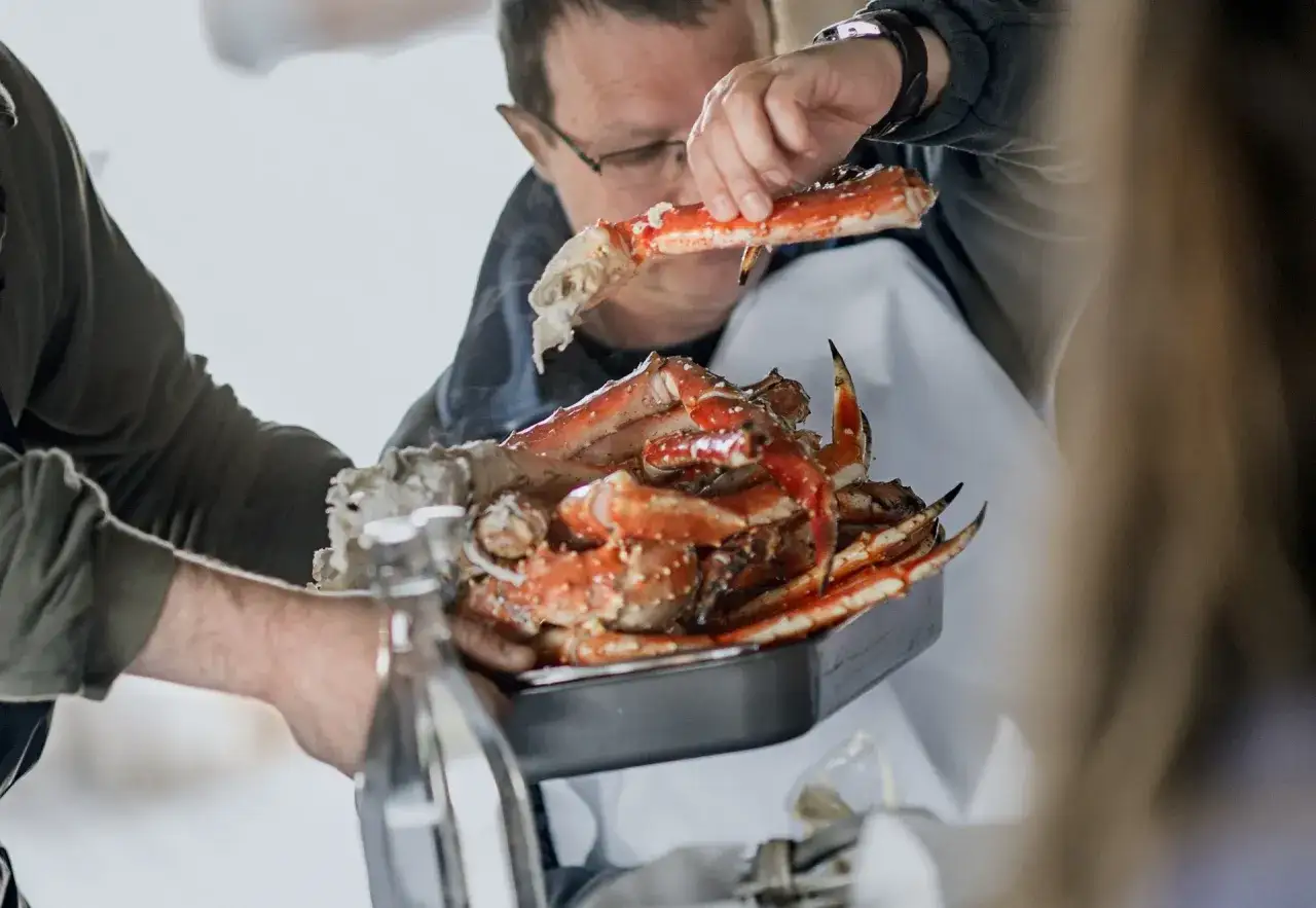 En man visar upp en stor kungskrabba från Norge. Den är tillagad och serveras i en form.