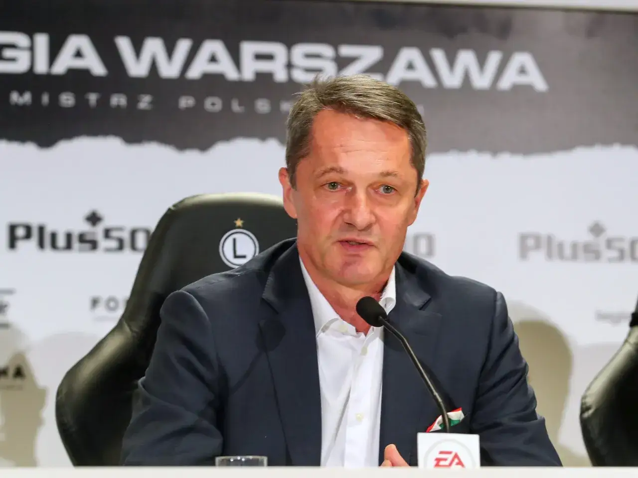 Dyrektor sportowy Legii, w garniturze, przemawia przy mikrofonie.