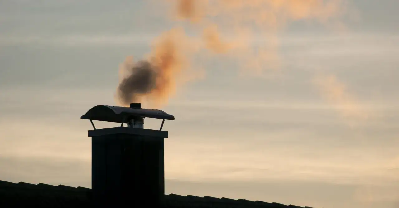 Humo oscuro y anaranjado sale de una chimenea sobre un tejado. El humo de la chimenea es malo para el aire que respiramos.