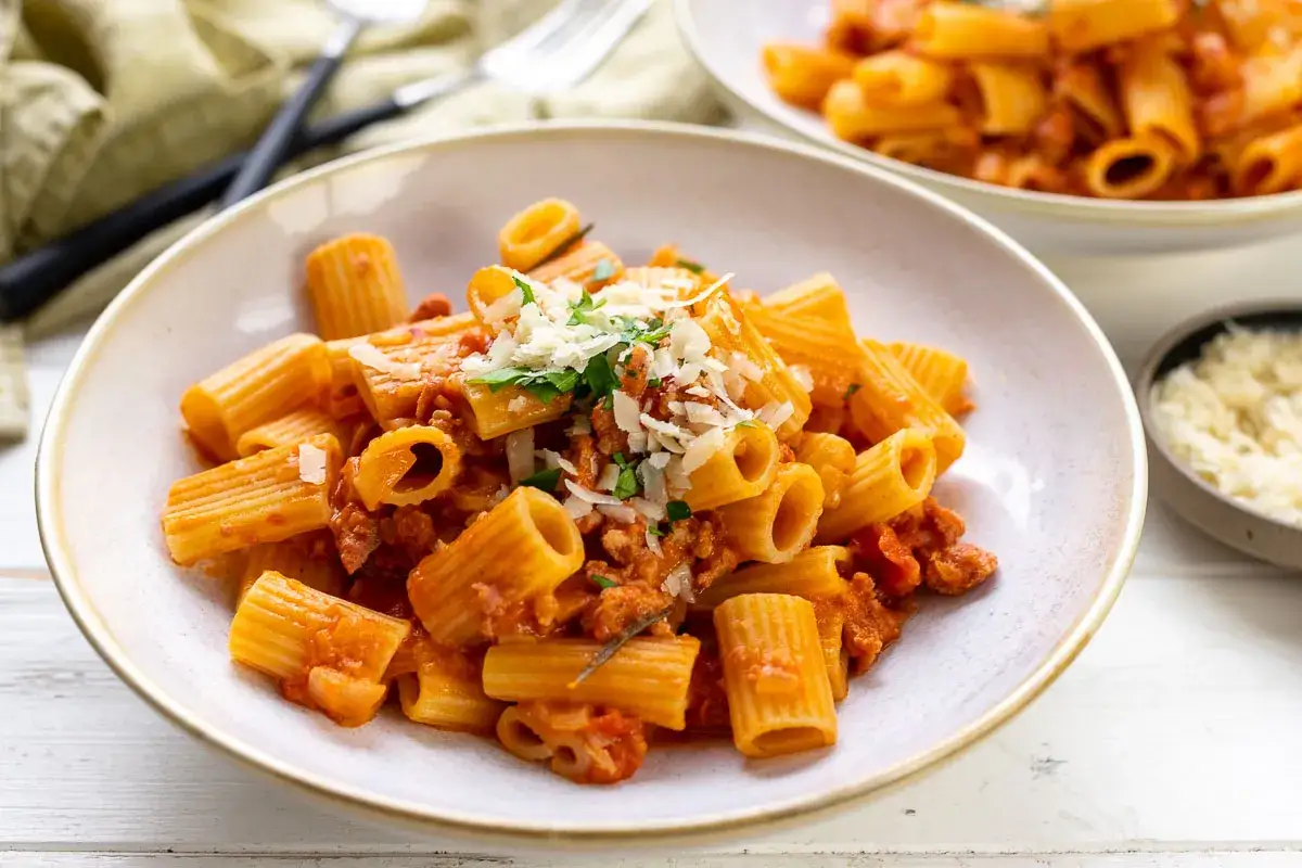 En skål med rigatoni pasta med en smakrik salsiccia-sås, toppad med riven parmesan och färsk persilja.