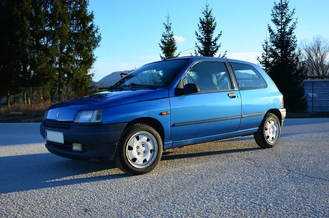 Niebieski Renault Clio z lat 90. na tle drzew i nieba. Idealny do kupna auta z Francji od handlarza.