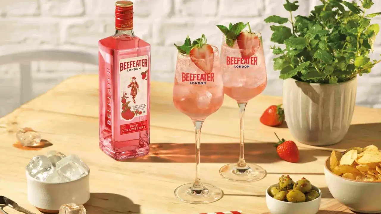 Tv&aring; glas med rosa drink med gin och prosecco, garnerade med jordgubbe och mynta. Bredvid st&aring;r en flaska Beefeater Pink Strawberry.