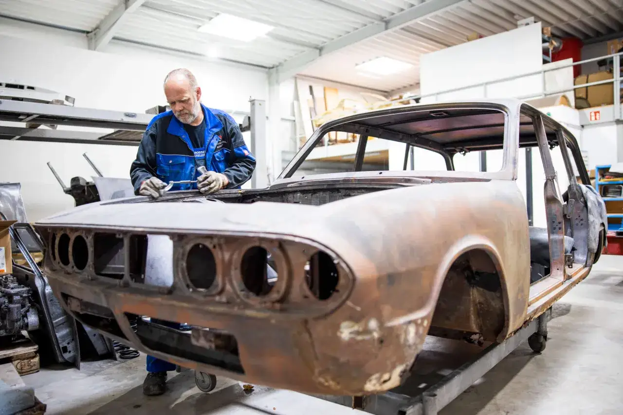 Mann arbeitet an rostiger Oldtimer-Karosserie. Die Kosten für das Oldtimer lackieren sind hoch, aber die Restaurierung lohnt sich.