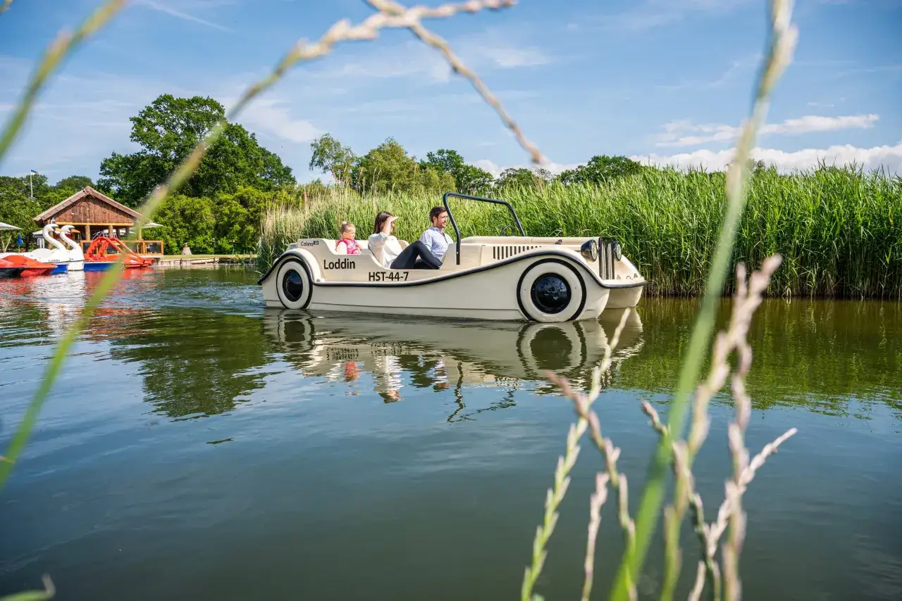Familie genießt eine Fahrt mit einem Auto-Boot von Kikis Bootsverleih auf einem ruhigen See, umgeben von grüner Natur.