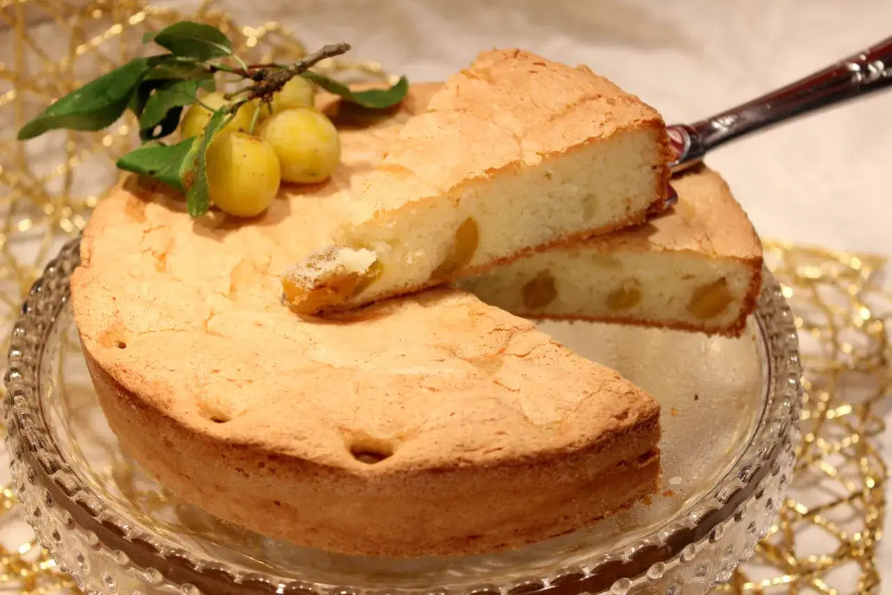 Gâteau lorrain aux mirabelles, une part coupée révèle les fruits dorés. Une branche de mirabelles décore ce délice.