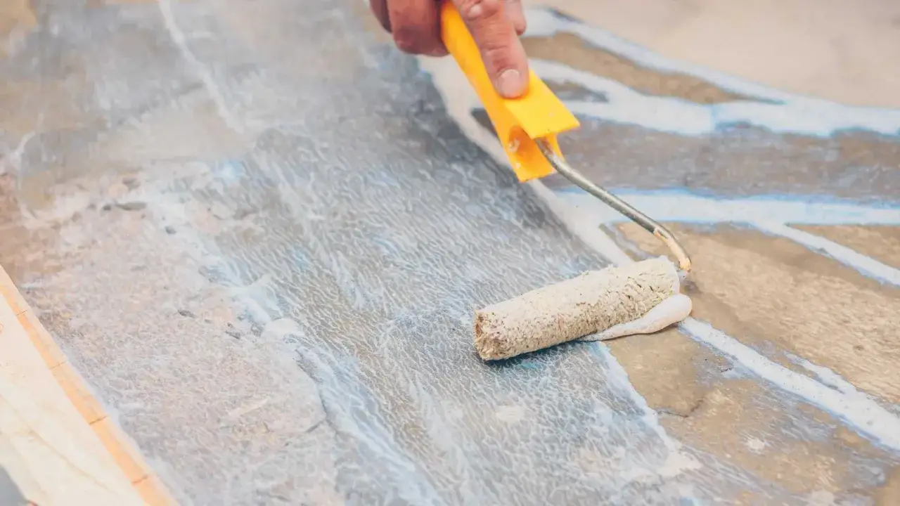 Application d'un primaire d'accrochage pour faïence avec un rouleau. Le produit blanc est étalé sur une surface grise et texturée.