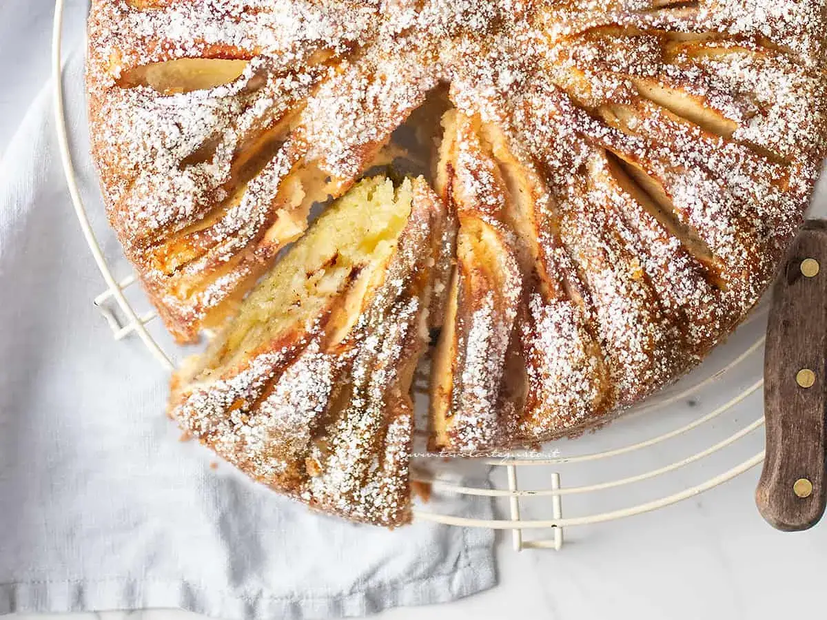 Deliziosa torta di mele in friggitrice ad aria, cosparsa di zucchero a velo, con una fetta tagliata che rivela la morbidezza.